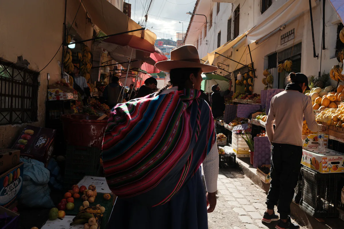 Eine Frau geht mit einem gestreiften Bündel auf dem Rücken durch eine Strasse in Cusco.
