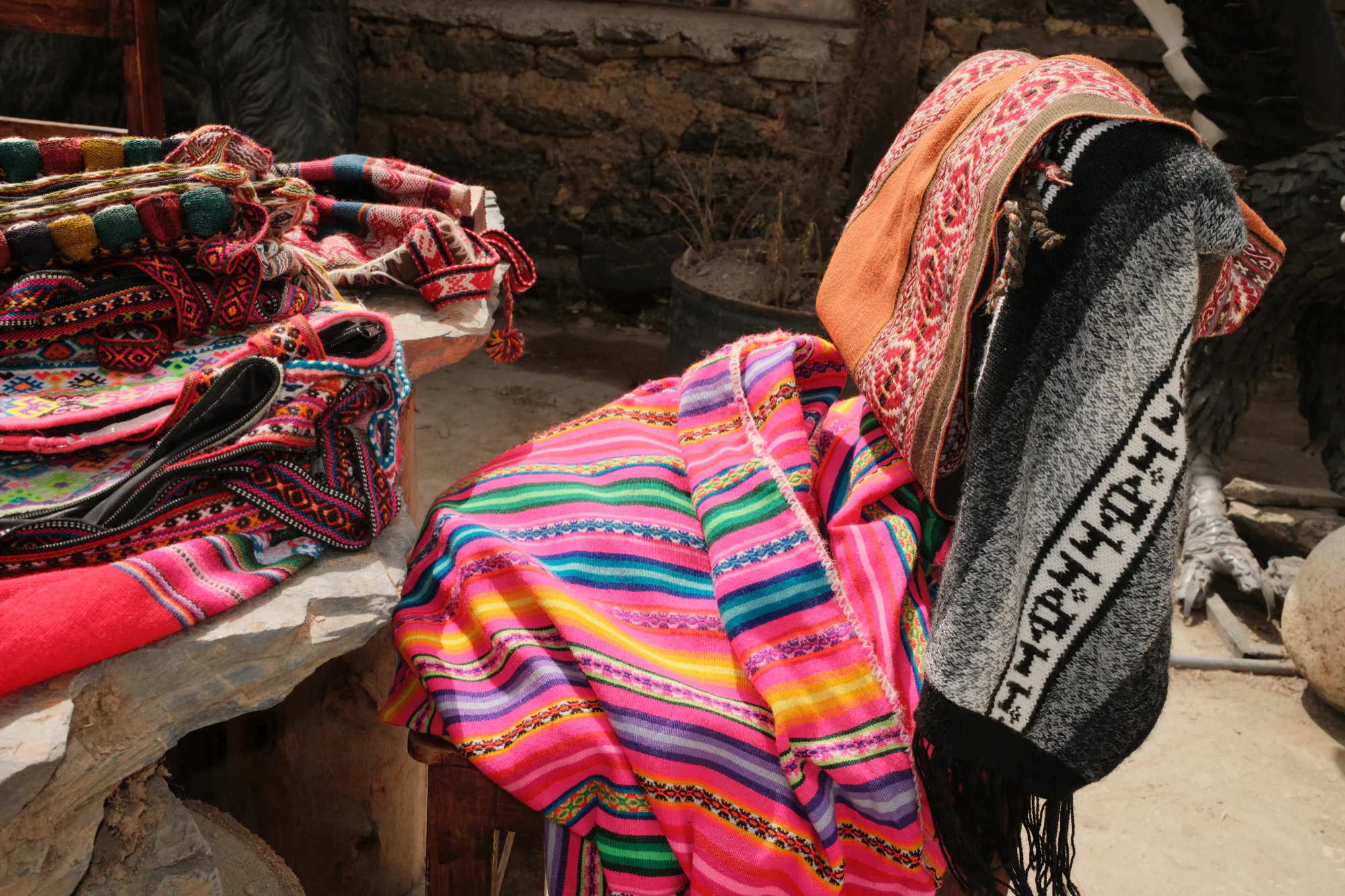 Leuchtend gemusterte Mantas, Bänder und touristische Textilwaren hängen dicht nebeneinander an einem Marktstand in Cusco.